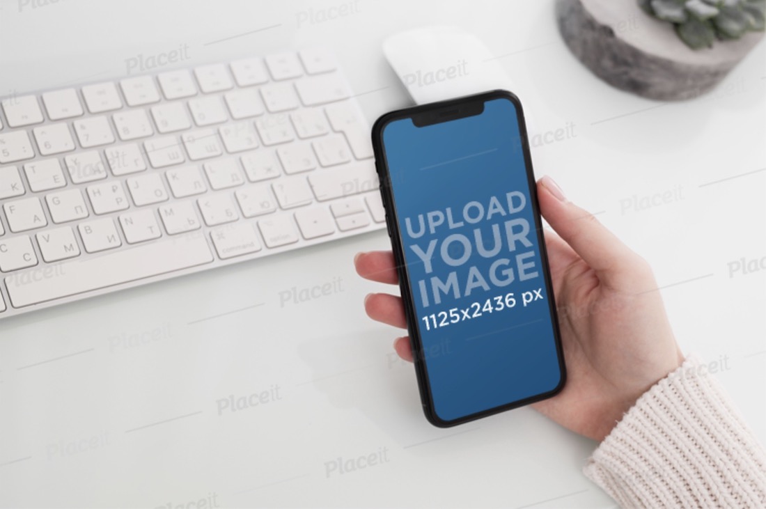 mockup featuring a woman's hand holding an iphone 11 pro over a neat desk